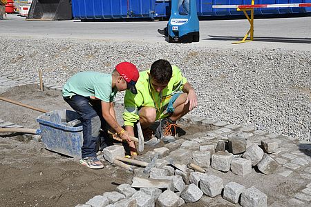 Am Tag der offenen Tür der EbiMIk Eröffnung, zeigt ein Mitarbeitender einem Kind wie man richtig Pflastersteine verbaut