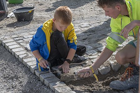 Am Tag der offenen Tür der EbiMIk Eröffnung, zeigt ein Mitarbeitender einem Kind wie man richtig Pflastersteine verbaut